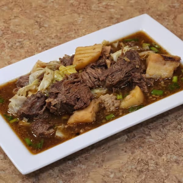 Hearty beef stew with cabbage and potatoes in a rich brown broth on a white rectangular plate.