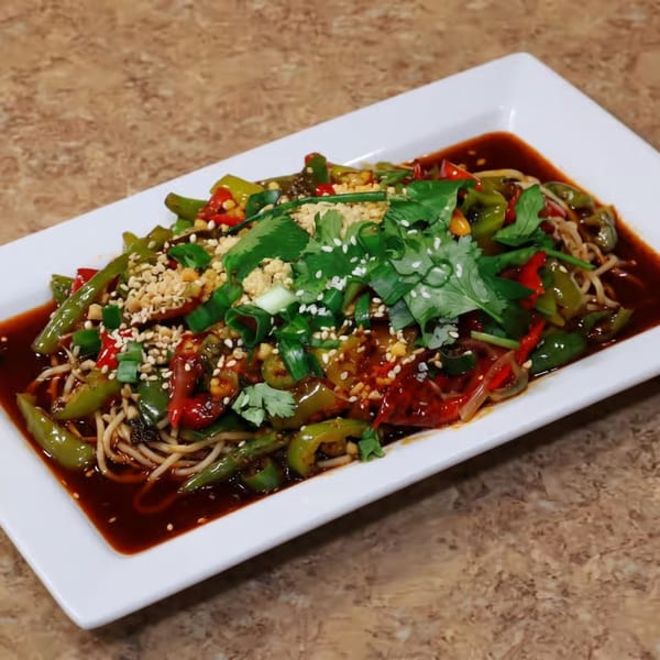 Noodles with green and red peppers, cilantro, sesame seeds, and peanuts in a dark sauce.
