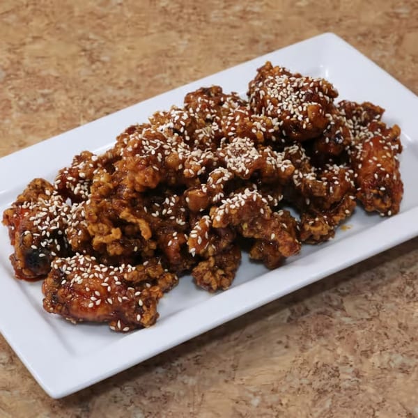 A white rectangular plate filled with crispy, glazed sesame chicken pieces on a brown countertop.