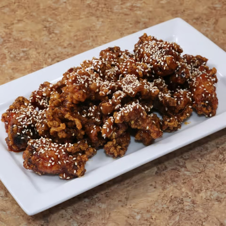 A white rectangular plate filled with crispy, glazed sesame chicken pieces on a brown countertop.