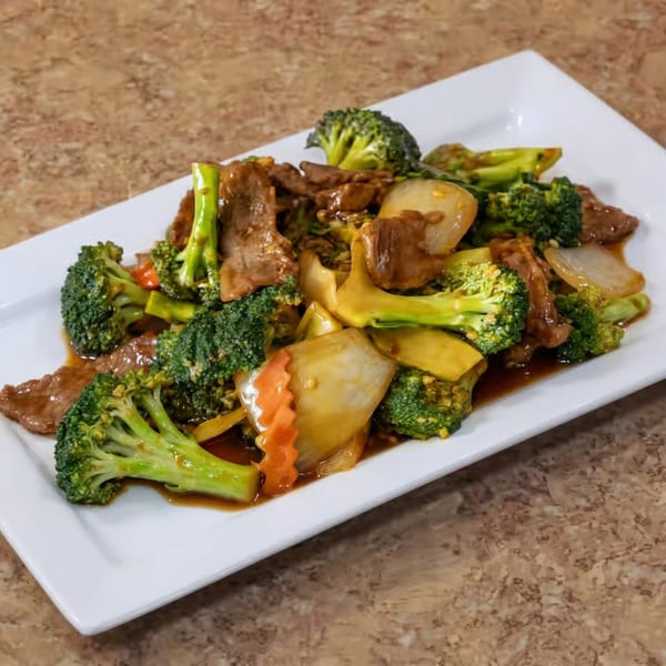 Beef and broccoli stir-fry with onions and carrots on a white rectangular plate.